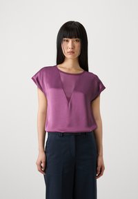 Blusa corta viola a maniche corte con scollatura a V profonda, realizzata in tessuto liscio. Ispiegata nei pantaloni neri a gamba larga. Design semplice e moderno.