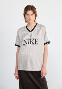 Gray Nike jersey with vertical stripes, v-neck, black trim, and a prominent black logo. Short sleeves and smooth texture.