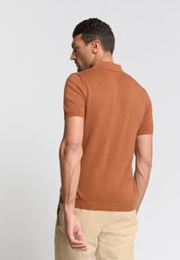Korte mouw polo-shirt in roestoranje breisel, met ribgebreide manchetten en een kraag. Gladde textuur met een aansluitende snit.
