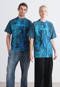 Grafisch bedruckte T-Shirts in Blau-Tönen mit abstrakten Mustern, kurzen Ärmeln und einer lockeren Passform. Der Stoff wirkt leicht.