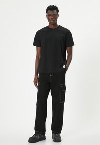 Camiseta de algodón negra con cuello redondo y mangas cortas, combinada con pantalones cargo negros que presentan bolsillos laterales y costuras blancas en contraste.
