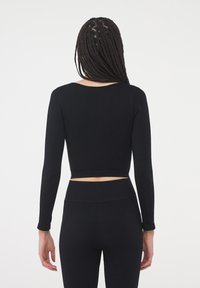 Czarny, długi rękaw, krótki top z okrągłym dekoltem, prążkowaną fakturą i dopasowanym krojem, w zestawieniu z pasującymi czarnymi legginsami z wysokim stanem.