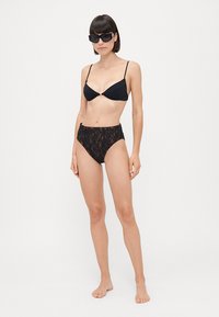 Ensemble bikini noir comprenant un haut triangle avec des fines bretelles et un bas taille haute en dentelle, les deux ayant une texture lisse.