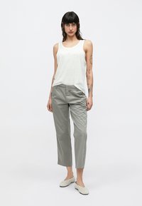 Pantalon gris clair et débardeur blanc. Le pantalon a une coupe décontractée et des poches ; le débardeur est ample avec une légère texture.