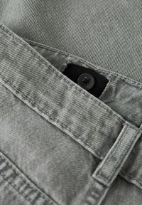 Primer plano de unos jeans de mezclilla gris con costuras detalladas y un botón negro parcialmente visible en la zona de la cinturilla.