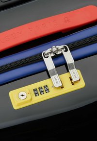 Valigia rigida nera con manico rosso, cerniera blu e lucchetto a combinazione giallo; zip in metallo con marchio inciso.