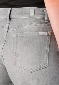Heledad hallid denim teksad, millel on lähedalt sobiv disain, tagakotid ja peened õmblusdetailid. Vöökoht on brändi sildiga.