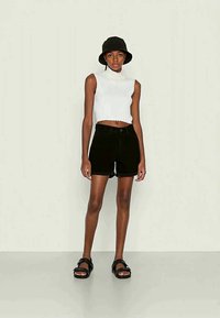 Μαύρα τζιν σορτς συνδυασμένα με λευκή ριμπαριστή αμάνικη μπλούζα, συμπληρωμένα με ένα μαύρο καπέλο μπέιζμπολ και μαύρες σαγιονάρες. Μινιμαλιστικός σχεδιασμός.