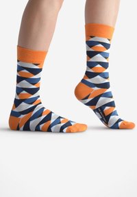 Chaussettes multicolores présentant un motif géométrique avec des formes orange, bleues et grises. Matériau en coton avec des poignets côtelés orange.