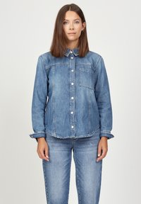 Denim shirt in light blue. Features a button-up front, collar, single chest pocket, and cuffed sleeves with a frayed edge.