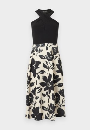 Μαύρο τοπ χωρίς μανίκια με λαιμόκοψη halter και λεπτομέρεια με σταυρωτό σχέδιο, συνδυασμένο με λευκή φούστα ψηλόμεση που φέρει μεγάλα μαύρα λουλουδένια σχέδια.