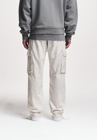 Beige cargo bukser med teksturfinish, med sidelommer og justerbare manchetter, parret med en grå sweatshirt.