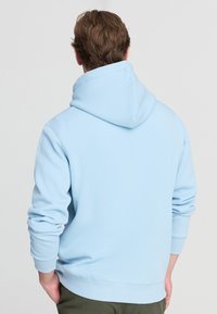 Felpa blu chiaro con cappuccio spazioso, polsini e cintura a coste. Tessuto morbido, vestibilità rilassata e dettagli di cucitura minimi.