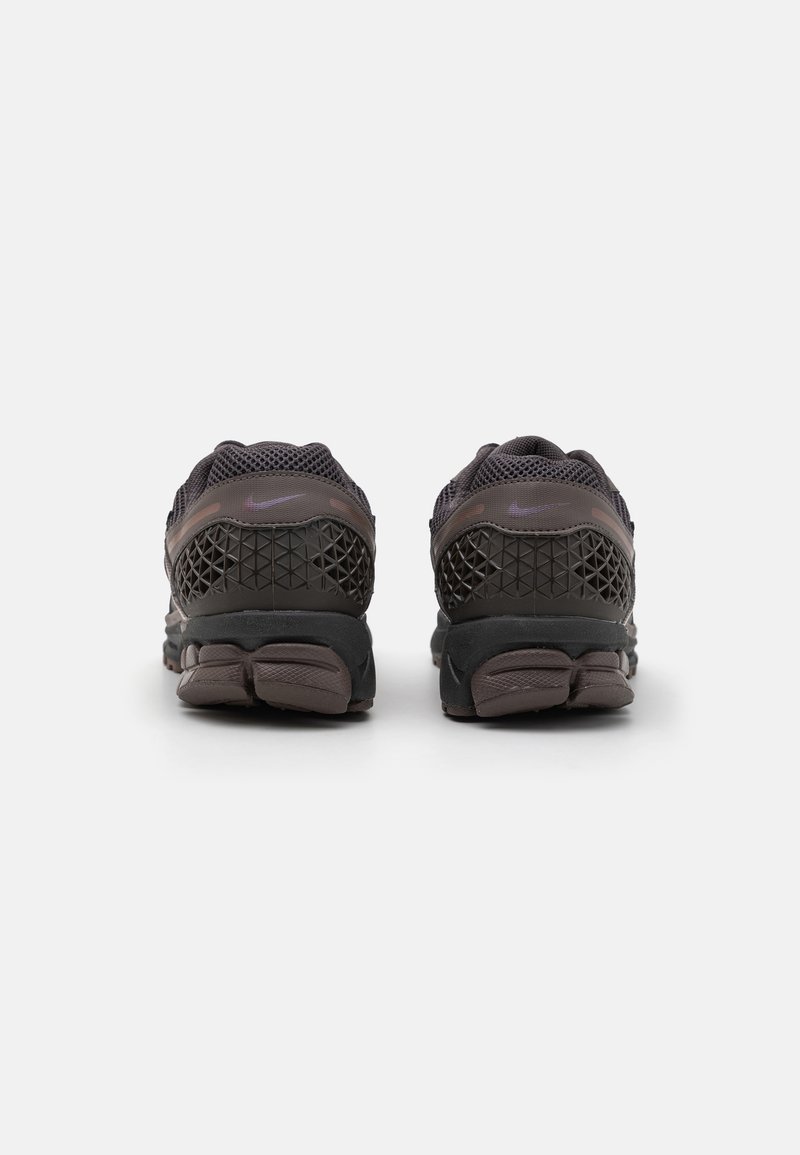 Donkergrijze atletiekschoenen met een mesh bovenkant, een gestructureerde hak en een rubberen zool met gesegmenteerde demping. Verfijnd met een subtiel logo op de achterkant.