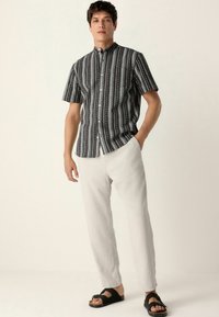 Cămașă cu mânecă scurtă, cu un model de dungi orizontale alb-negru, asortată cu pantaloni largi de culoare deschisă și sandale negre cu bretele.