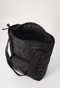 Black fabric tote bag with a textured surface, zip closure, and a small front pocket. Features sturdy straps and a spacious interior.