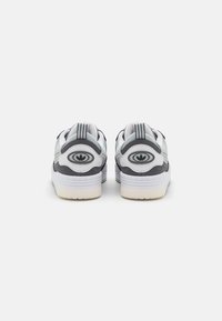 Obuwie z szaro-białą cholewką o gładkiej teksturze, wyściełanym kołnierzem i uniesionym detalem logo. Gumowa podeszwa z wzorem.