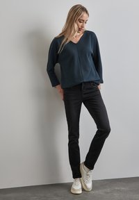 Laivastonsininen ribattu pitkähihainen toppi V-päällä, yhdistettynä mustiin slim-fit-farkkuihin ja valkoisiin tennareihin, joissa on tanssiväriset yksityiskohdat. Yksinkertainen, rento asu.