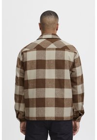 Brown and beige plaid shirt jacket with a buttoned collar, long sleeves, and a straight cut. Textured fabric features large squares.