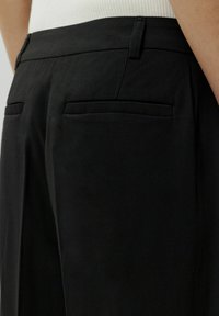 Schwarze Hose mit einer glatten Stofftextur, zwei Gesäßtaschen und einer taillierten Passform. Gerader Beinverlauf mit subtilen Nähten.