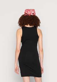 Vestido preto sem mangas com silhueta ajustada e decote redondo, emparelhado com um lenço vermelho estampado atado nas costas.