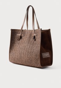 Hnedá tkaná taška cez rameno s koženými remienkami, s textúrovaným dizajnom pripomínajúcim slamu a tmavým semišovým bočným panelom s menovkou značky.