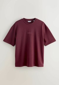 Burgundy cotton t-paita, jossa on lyhyet hihat ja pyöreä kaula-aukko, etupuolella pieni painettu teksti "Melrose Ave". Sujuva pinta.