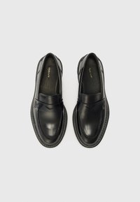 Mocassins en cuir noir avec une finition lisse, présentant une sangle décorative sur le devant et des coutures contrastées le long de la semelle.