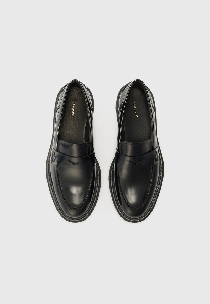 Svarta läderskor med slät yta, med ett dekorativt band över framsidan och kontrasterande sömmar längs sulan.