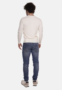 Maglione lavorato a maglia beige chiaro con maniche lunghe, abbinato a jeans in denim blu. Il maglione presenta un collo a giro e orlo a coste.