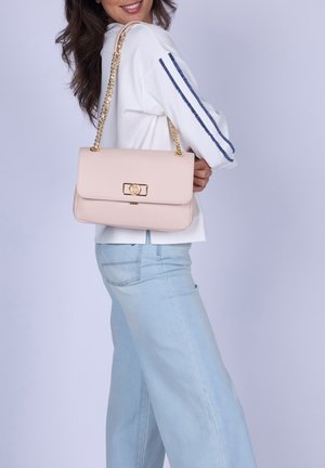 Donna che indossa un maglione bianco con strisce blu e jeans azzurri, con una borsa rosa chiaro con tracolla a catena dorata sulla spalla.