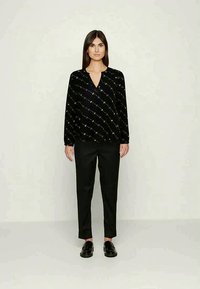 Blusa preta de manga longa com decote em V e padrão abstrato multicolorido, combinada com calças pretas de perna reta e mocassins pretos.