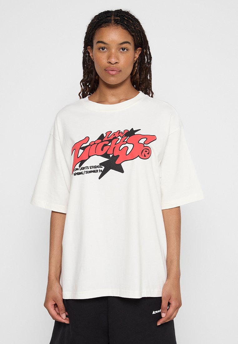 T-shirt oversized blanc à manches courtes, avec un imprimé graphique rouge et noir sur le devant. Fabriqué en coton, avec une texture douce.
