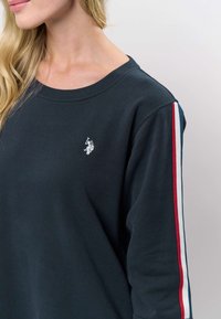 Marineblauer Pullover mit Rundhalsausschnitt, verziert mit weißer Stickerei und gestreiften Akzenten in Rot, Weiß und Blau entlang der Ärmel.