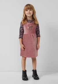 Rosenrotes Corduroy-Kleid mit Trägern, verziert mit floralen Stickereien; kombiniert mit einem langärmligen schwarzen Blumenthemenhemd und schwarzen Schnürstiefeln.