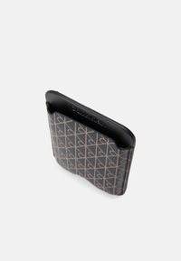 Porte-cartes en cuir noir avec un motif de cœur géométrique beige, texture lisse et bords arrondis, avec un logo embossé discret.