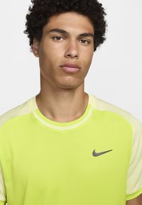 Camiseta atlética de manga corta de color amarillo brillante con un tejido texturizado y acentos en un amarillo claro en los hombros. Presenta un pequeño logo negro de Nike.