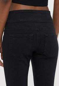 Črne visokopasne kavbojke z gladko teksturo, z dvema zadnjima žepoma in subtilnim šivanjem ob pasu in žepih.