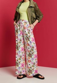 Wijduitlopende bloemenbroek in het wit, met roze, groene en paarse patronen. Gecombineerd met een lichtgroene geribbelde top en een olijfgroene jas.