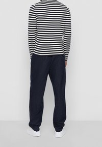 Långärmad randig skjorta i marinblått och vitt, tillsammans med en lös passform av mörka denimbyxor. Vita sneakers fulländar outfiten.