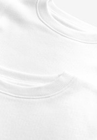 T-shirts en coton blanc avec cols ronds côtelés. La vue en gros plan montre une texture lisse et un subtil motif en croix sur le tissu.