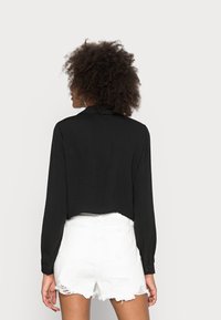 Schwarzes, langärmeliges, kurzes Hemd mit Kragen, kombiniert mit weißen, distressierten Shorts mit fransigem Saum und Gesäßtaschen.