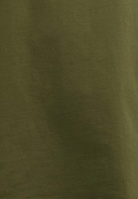 Tissu en coton de couleur vert olive avec une texture douce, présentant une surface uniforme et des variations subtiles de ton. Pas de motifs ou d'accents distincts.