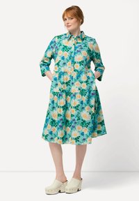 Abito floreale con sfondo verde-azzurro, con bottoni anteriori, maniche arrotolate e gonna a strati. Abbinalo a zoccoli platform di colore chiaro.