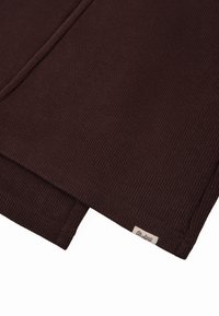 Tissu tricoté marron foncé avec une texture côtelée, replié sur les bords, portant une petite étiquette tissée avec "Oh Aponi."