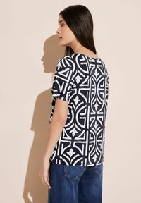 Navyblauer Kurzarm-Top mit einem auffälligen weißen geometrischen Muster. Der Stoff hat eine glatte Textur, und das Design bedeckt die gesamte Oberfläche.