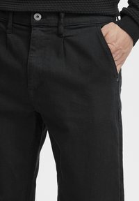 Black denim trousers with a relaxed fit, featuring front pockets, a button closure, and a textured waistband for added grip.