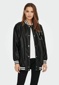 Jachetă varsity din piele sintetică neagră, cu guler și manșete ribbate albe cu dungi, având o mare literă albă „W” pe față.