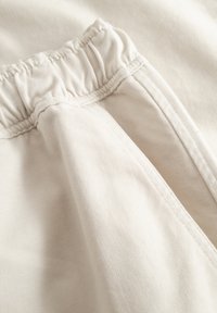 Gros plan sur un pantalon beige clair avec une taille élastique et des coutures visibles le long de la couture latérale et du bord de la poche.
