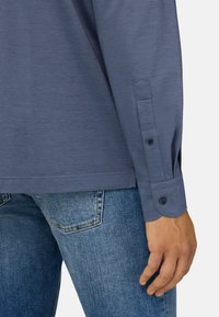 Langarm overhemd in donkerblauwe stof met een gladde textuur, voorzien van knoopmanchetten en een rechte zoom, gecombineerd met lichtblauwe jeans.